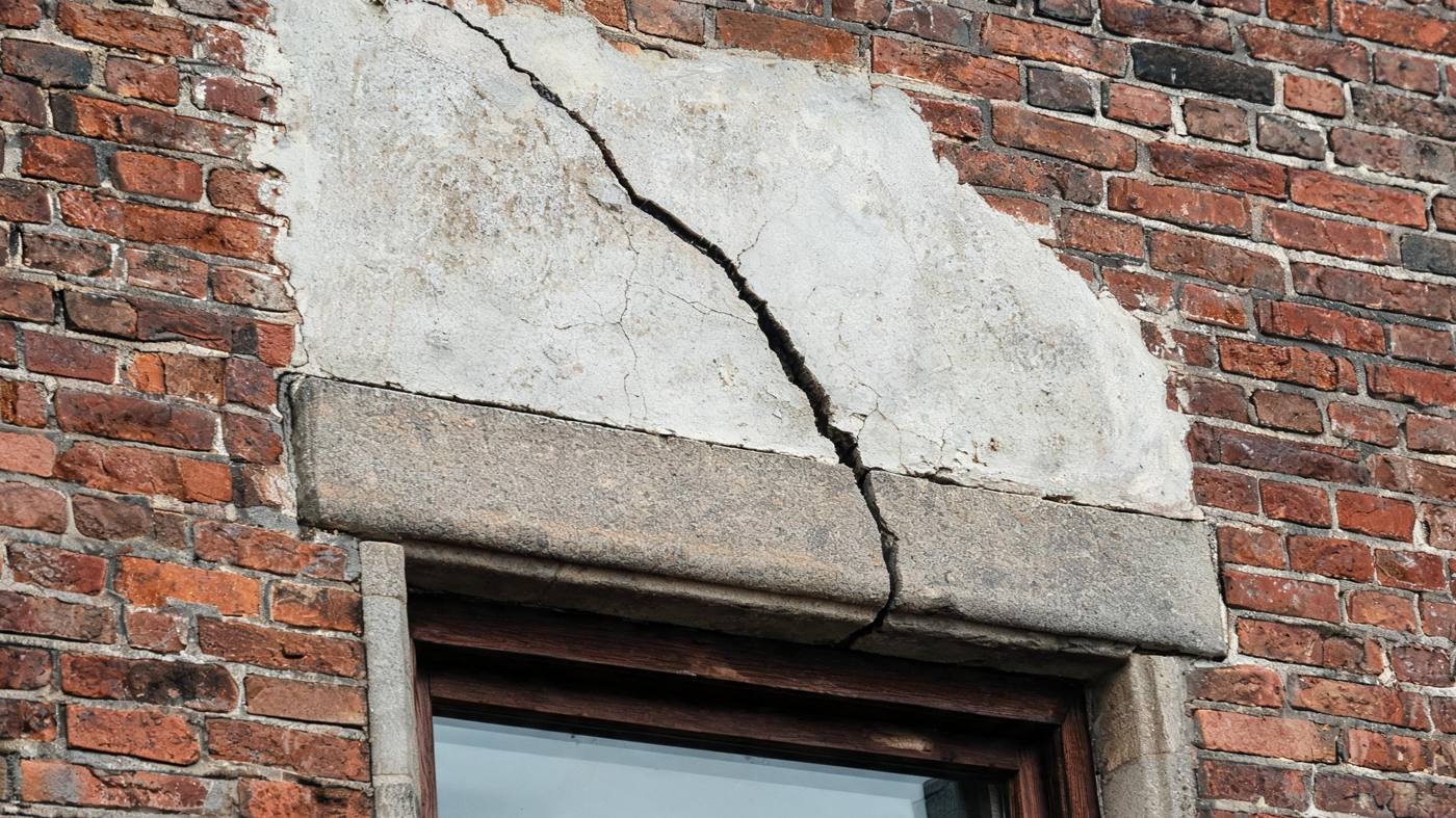Diagonaler Riss im Putz über einem Fenstersturz eines älteren Wohnhauses